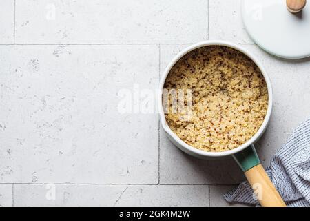 Quinoa cotta in casseruola, sfondo piastrellato grigio, vista dall'alto. Concetto di cibo sano. Foto Stock