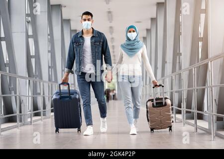 Viaggi durante Pandemic. Coppia islamica che indossa maschere a piedi con valigie all'aeroporto Foto Stock