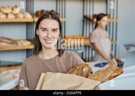 Ritratto di sorridente giovane cliente che tiene fresco pane cotto in sacchetto con l'aperbag contro stalla Foto Stock