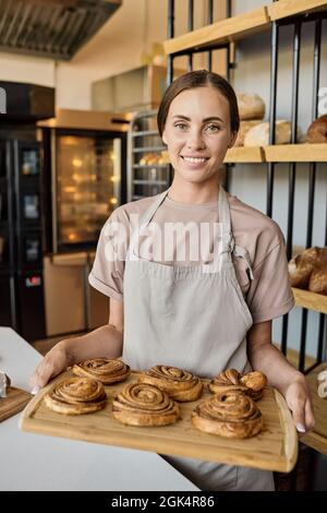 Ritratto di giovane ragazza felice panettiere in piedi sul posto di lavoro e vendere pasticceria fresca Foto Stock