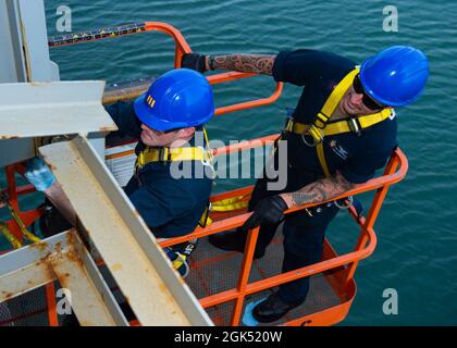 210803-N-LK667-0228 TEMA, Ghana (agosto 3, 2021) Aviation Boatswain's Mate (Fuels) Airman Bradley A. Lawson, a sinistra, applica grasso lubrificante a una cerniera, mentre Aviation Support Equipment Technican 1st Class Stephen B. Sorenson controlla un sollevatore JLG a bordo della base navale di Expeditionary USS Hershel 'Woody' Williams (ESB 4), 3 agosto 2021. Hershel 'Woody' Williams è in fase di dispiegamento programmato nell'area della Sixth Fleet degli Stati Uniti di operazioni a sostegno degli interessi e della sicurezza nazionali degli Stati Uniti in Europa e Africa. Foto Stock