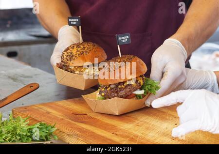 Uno chef prepara un hamburger per un cliente. Un uomo che indossa guanti di protezione bianchi raccoglie una scatola di hamburger da consegnare a un cliente. Foto Stock