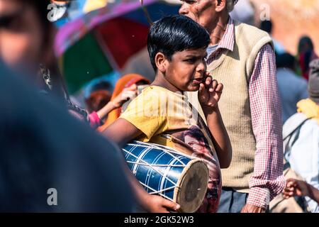 Orchha, Madhya Pradesh, India - Marzo 2019: Un candido ritratto di strada di un giovane ragazzo indiano che tiene un tamburo musicale in una strada affollata. Foto Stock