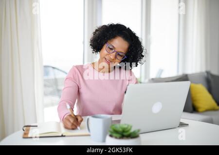 Ritratto di donna matura felice che lavora su notebook in ambienti chiusi, concetto di ufficio domestico. Foto Stock