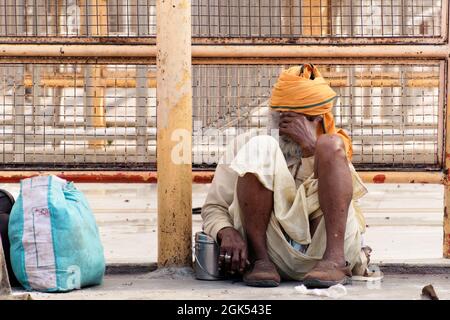 Orchha, Madhya Pradesh, India - Marzo 2019: Un uomo indiano vecchio che indossa un turban arancione seduta triste e preoccupato fuori delle recinzioni di un tempio indù i Foto Stock