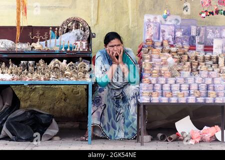 Orchha, Madhya Pradesh, India - Marzo 2019: Una donna indiana venditore di strada che si siede pensieroso al suo stallo stradale che vende i fiangoli in un mercato. Foto Stock