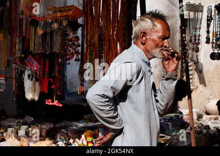 Orchha, Madhya Pradesh, India - Marzo 2019: Un uomo indiano anziano che si trova fuori da un negozio e fuma una sigaretta bidi. Foto Stock