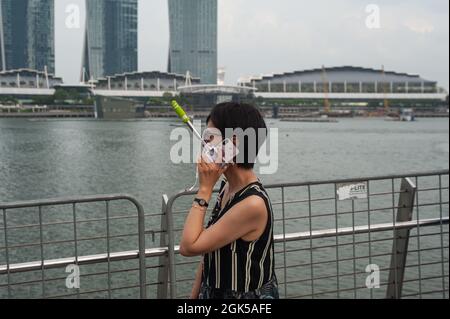 03.08.2018, Singapore, Repubblica di Singapore, Asia - Una donna cammina lungo il lungomare di Marina Bay e parla sul suo telefono cellulare. Foto Stock