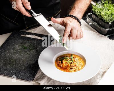 Autentica paella spagnola con merluzzo e cozze. Tradizionale piatto di pesce mediterraneo. Lo chef aggiunge verdure al piatto. Piatti del ristorante. Clos Foto Stock