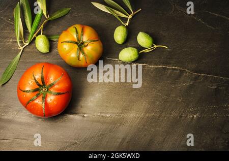 Natura morta con due pomodori e olive coltivati in modo biologico, simboli della dieta mediterranea, su sfondo scuro con spazio per la copia a destra del Foto Stock