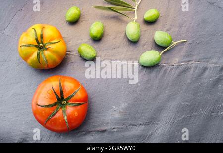 Natura morta con due pomodori e olive coltivati in modo biologico, simboli della dieta mediterranea, su sfondo scuro con spazio per la copia a destra del Foto Stock
