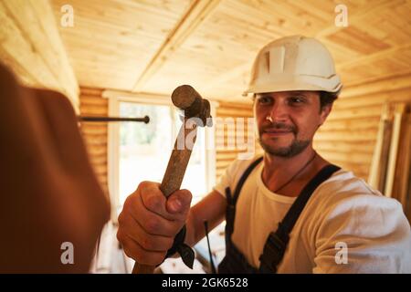 Costruttore diligente martellando in un chiodo in parete di legno Foto Stock