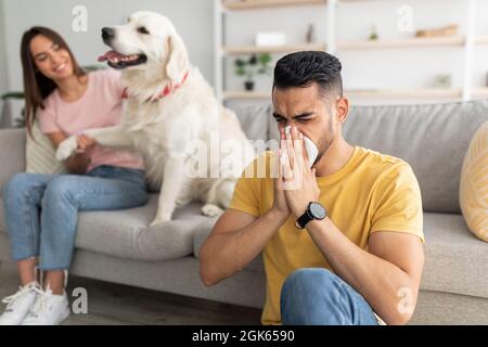 Malato arabo ragazzo che ha freddo, soffia naso, starnuti in carta tissue, la sua ragazza con cane da compagnia su sfondo, copia spazio Foto Stock