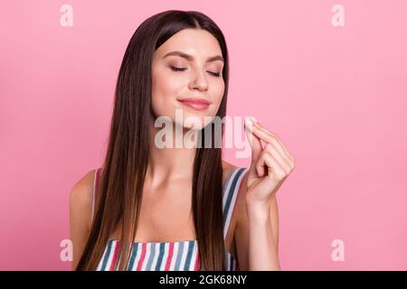 Ritratto di attraente marrone-capelli sognante ragazza allegra degustazione buon cibo isolato su sfondo rosa pastello colore Foto Stock