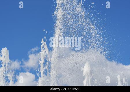 Diversi ruscelli verticali di acqua si alzano e si schizzano contro il cielo blu nuvoloso estivo. Foto Stock