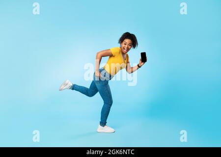 Felice giovane afrodonna con smartphone vuoto su sfondo blu, mockup per sito web o app mobile Foto Stock