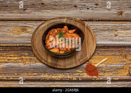 Delizioso pollo stufato con prezzemolo e pepe su piatto di legno e cucchiaio con paprika Foto Stock
