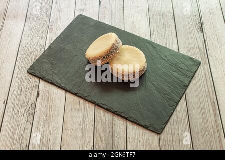 Piatto di ardesia di mini alfajores argentino cosparso di cocco su tavolo di legno chiaro Foto Stock