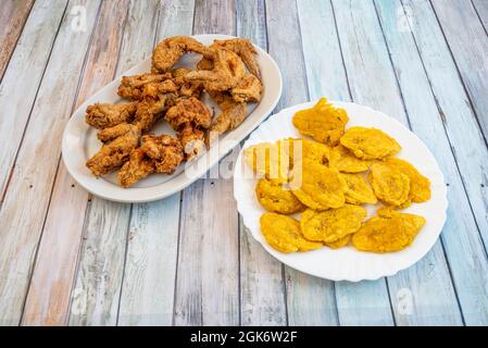 Grande porzione di ali di pollo impanate su un vassoio bianco e con patatine fatte in casa a base di banane mature come guarnitura Foto Stock