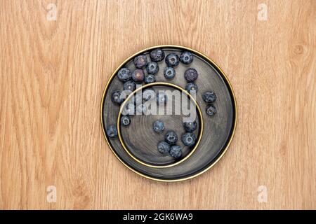 vista dall'alto di una manciata di mirtilli maturi all'interno di piatti di metallo d'epoca su un tavolo di quercia Foto Stock