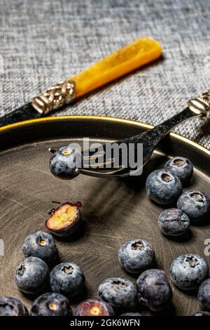 Mirtilli maturi in cima a un piatto di metallo d'annata, uno dei mirtilli trafitto da una forchetta e l'altro tagliato a metà Foto Stock