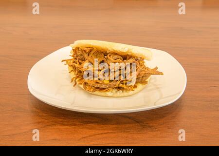 Arepa venezuelana di carne grattugiata con pasta di mais su piastra bianca Foto Stock