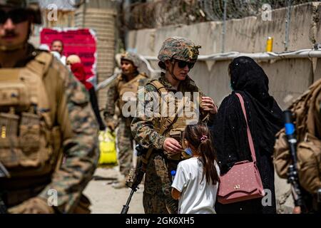 Una Marina assiste una donna e un bambino durante un'evacuazione all'Aeroporto Internazionale Hamid Karzai, 18 agosto. I membri del servizio degli Stati Uniti stanno assistendo il Dipartimento di Stato con un prelievo ordinato di personale designato in Afghanistan. Foto Stock