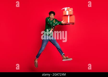 Foto di funky sportivo tipo salto portare pile giftboxes urlo bocca aperta indossare il maglione cervi verde isolato su sfondo rosso Foto Stock