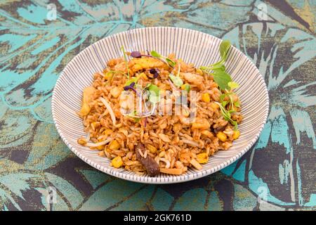 Stufato di riso orientale con funghi asiatici, germogli di fagioli, germogli vegetali, mais dolce e soia in un piatto grattugiato Foto Stock