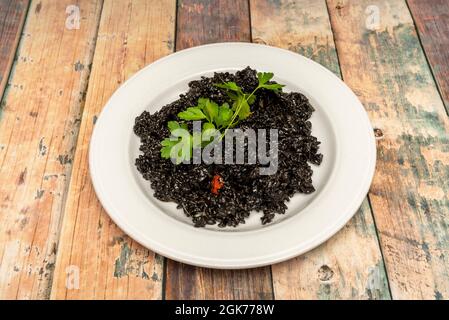 Porzione di paella nera spagnola con prezzemolo in cima per servire come tapas su tavola di legno Foto Stock