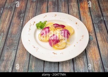 Porzione di merluzzo alla griglia con patate bollite e pezzi di cipolla rossa su un piatto bianco Foto Stock