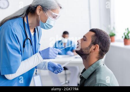 medico asiatico di mezza età in maschera medica facendo test pcr per il giovane in ospedale Foto Stock