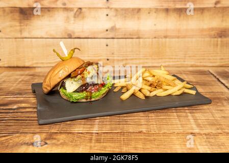 Delizioso hamburger di manzo messicano con formaggio fuso, jalampeños, lattuga, guacamole e salsa barbecue con un lato di patatine fritte Foto Stock