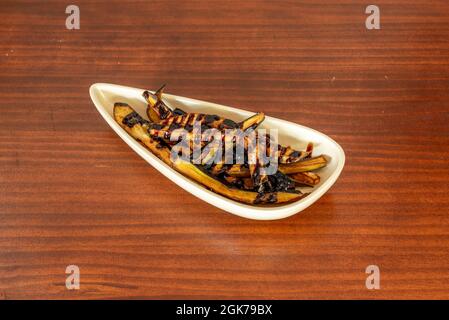 Strisce di melanzane, in quantità, pastellate con sciroppo di zucchero di canna su un vassoio bianco e una tavola color ciliegia Foto Stock