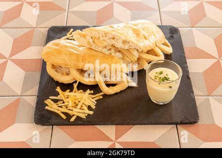 Popolare panino di anelli di calamari pastoriati e fritti in olio d'oliva spagnolo con salsa di maionese tagliata a metà. Foto Stock