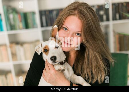 Felice donna proprietario di jack russell terrier cane, si sente la responsabilità di prendersi cura di animali domestici, in piedi contro scaffali sfondo. Persone e. Foto Stock