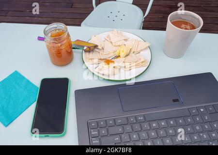 Telelavoro e fare colazione davanti al pc con caffè con latte e pane con burro e marmellata d'arancia amara Foto Stock
