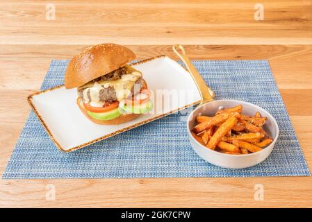 Hamburger con formaggio, cipolla, pomodoro e avocado accompagnati da un recipiente bianco pieno di patate dolci Foto Stock