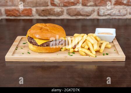 Hamburger di manzo classico con formaggio cheddar fuso guarnito con patatine fritte e salsa da bagnare Foto Stock