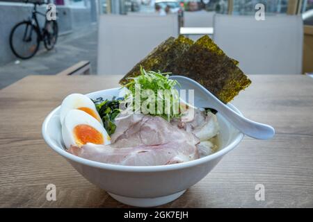 Shio Ramen, zuppa di vongole Japaneses, sopra con maiale, uovo sodo, germogli di bambù, cipolla rossa e Nori, su tavolo esterno in legno. Foto Stock