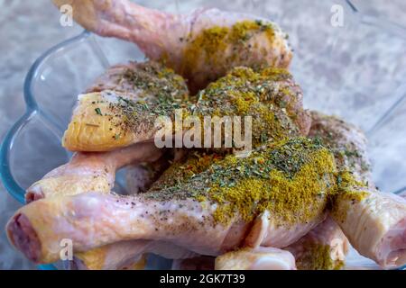 Cosce di pollo crude mescolate con varie spezie. I bastoncini di pollo non cotti sono preparati per essere cucinati. Foto Stock