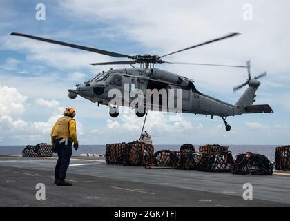 OCEANO PACIFICO (30 agosto 2021) un falco marino MH-60S, attaccato a Helicopter Sea Combat Squadron (HSC) 25, conduce un rifornimento verticale (VERTREP) con nave d'assalto anfibio USS Essex (LHD 2), agosto 30. L'Essex, ammiraglia dell'Essex Amphibious Ready Group (ARG), insieme all'XI Marine Expeditionary Unit (MEU), opera nell'area di responsabilità della settima flotta statunitense per migliorare l'interoperabilità con alleati e partner e fungere da pronta forza di reazione per difendere la pace e la stabilità nella regione indopacifica. Foto Stock