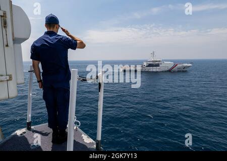 Un membro dell'equipaggio della Guardia Costiera degli Stati Uniti Cutter Munro saluta un vascello della Guardia Costiera delle Filippine che transita lungo il Munro nel Mare delle Filippine Occidentali, 31 agosto 2021. I membri della Guardia Costiera a bordo del Munro e della Guardia Costiera filippina hanno partecipato ad operazioni ed esercizi bilaterali che includevano comunicazioni e ricerca e salvataggio. Foto Stock