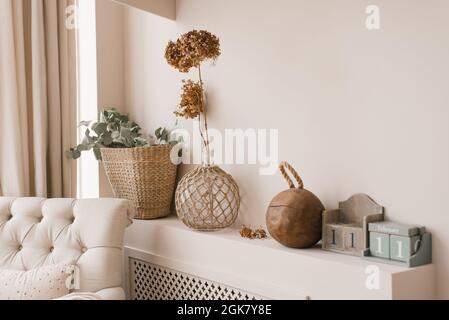 Decorazioni scandinave come decorazione nella casa. Fiori essiccati di hydrangea in un vaso, rami di eucalipto in un cestino di vimini su una mensola nel roro vivente Foto Stock