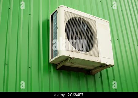 Aria condizionata a parete. Aria condizionata all'esterno del negozio. Parete verde in lamiera profilata e dispositivo di raffreddamento bianco con ventola. faci industriale Foto Stock