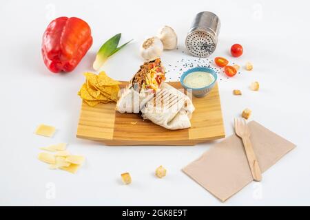 Burrito ripieno di peperoncino con carne, formaggio grattugiato e Pico de gallo con tortilla di grano e nachos di mais con salsa di avocado Foto Stock