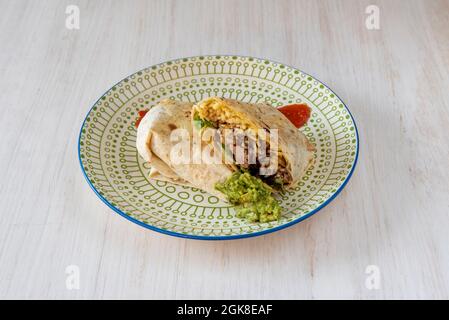 Tortilla burrito di frumento ripiena di chipotle di pollo, guacamole e riso con salse su piatto decorato Foto Stock