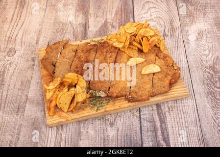 Cachopo di manzo con prosciutto e formaggio pastellato con farina, uova e pangrattato e una guarnitura di patate fritte in patatine fatte in casa Foto Stock