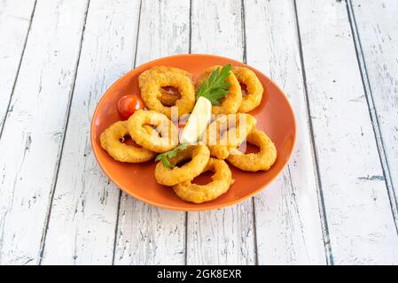 Tapa di calamari lavorati in pastella su piatto arancione con limone e prezzemolo e fondo bianco Foto Stock