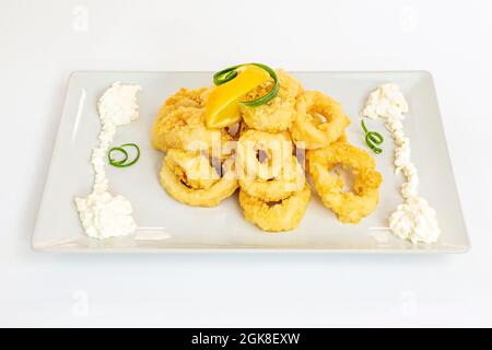 Calamari in stile romano, pronti a mangiare in un ristorante di tapas spagnole, guarniti con maionese e formaggio su un piatto bianco Foto Stock